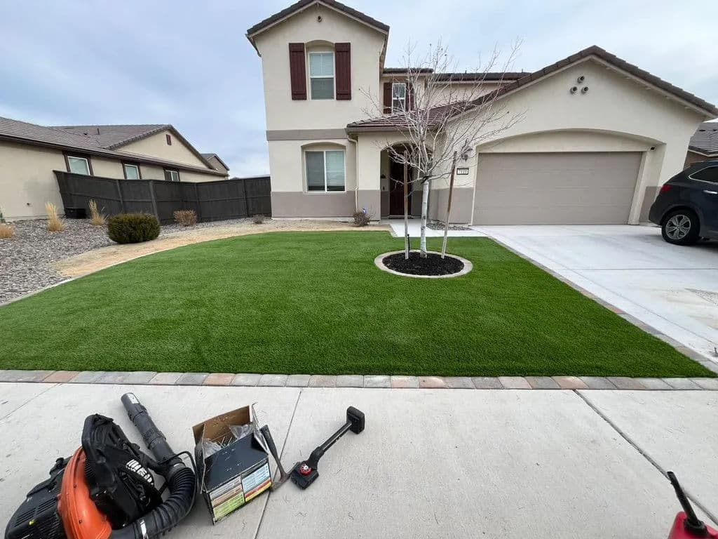Well-maintained front yard with artificial grass, a small tree, and clean driveway near a suburban home.