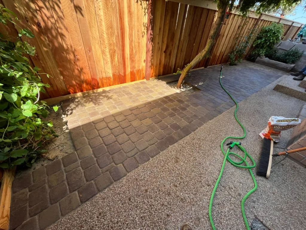 Newly paved garden walkway with cobblestone pattern, surrounded by greenery and a wooden fence.
