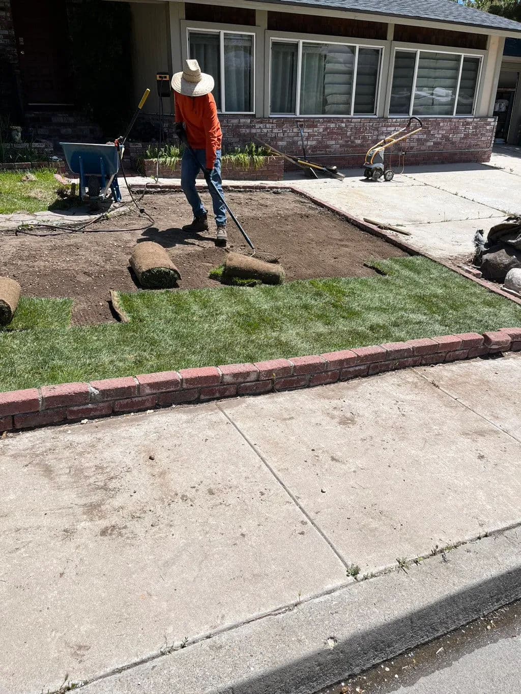 Gardener laying sod in front yard, using tools and preparing the ground for grass installation.