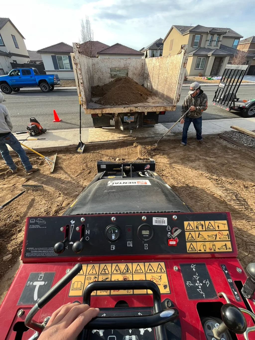 View from a soil compactor with workers unloading dirt from a truck at a construction site.