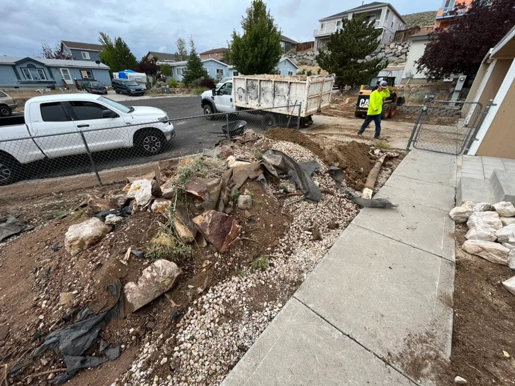 Construction site with worker, gravel, and equipment near residential homes.