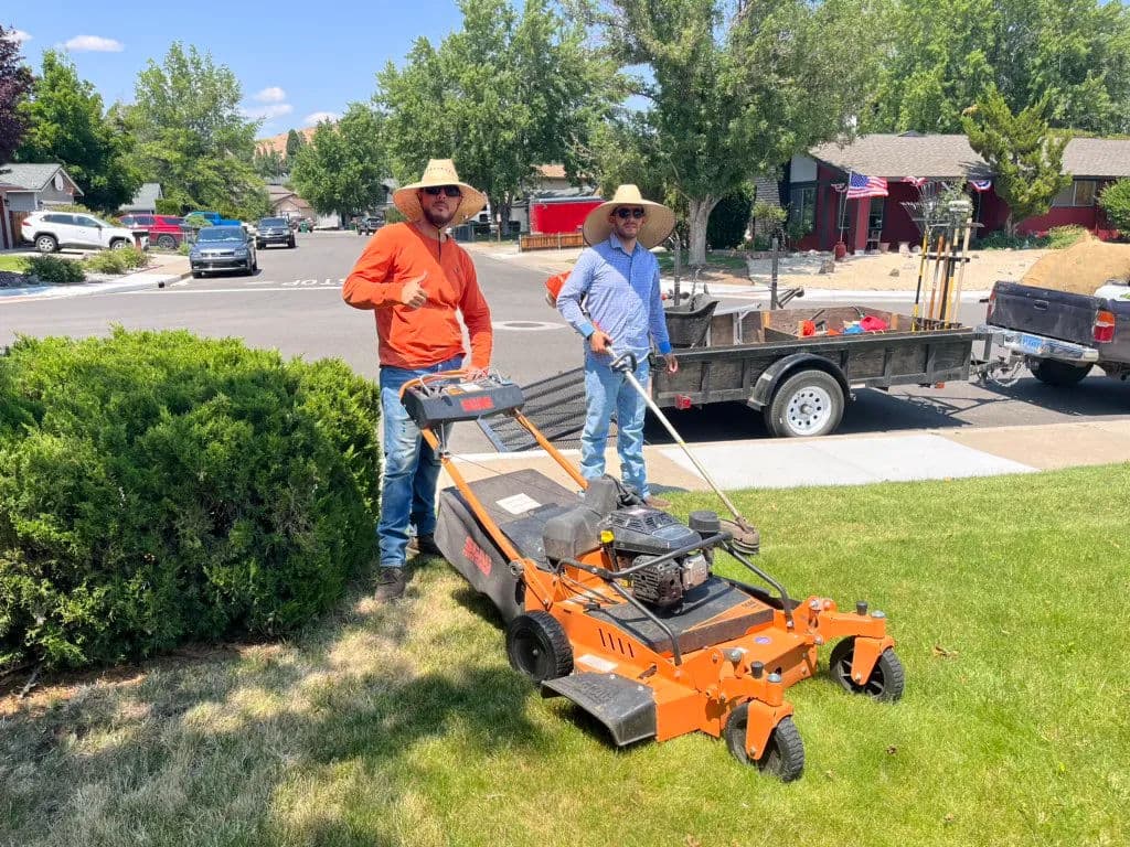 Two landscapers using a grass cutter on a sunny day in a suburban neighborhood.