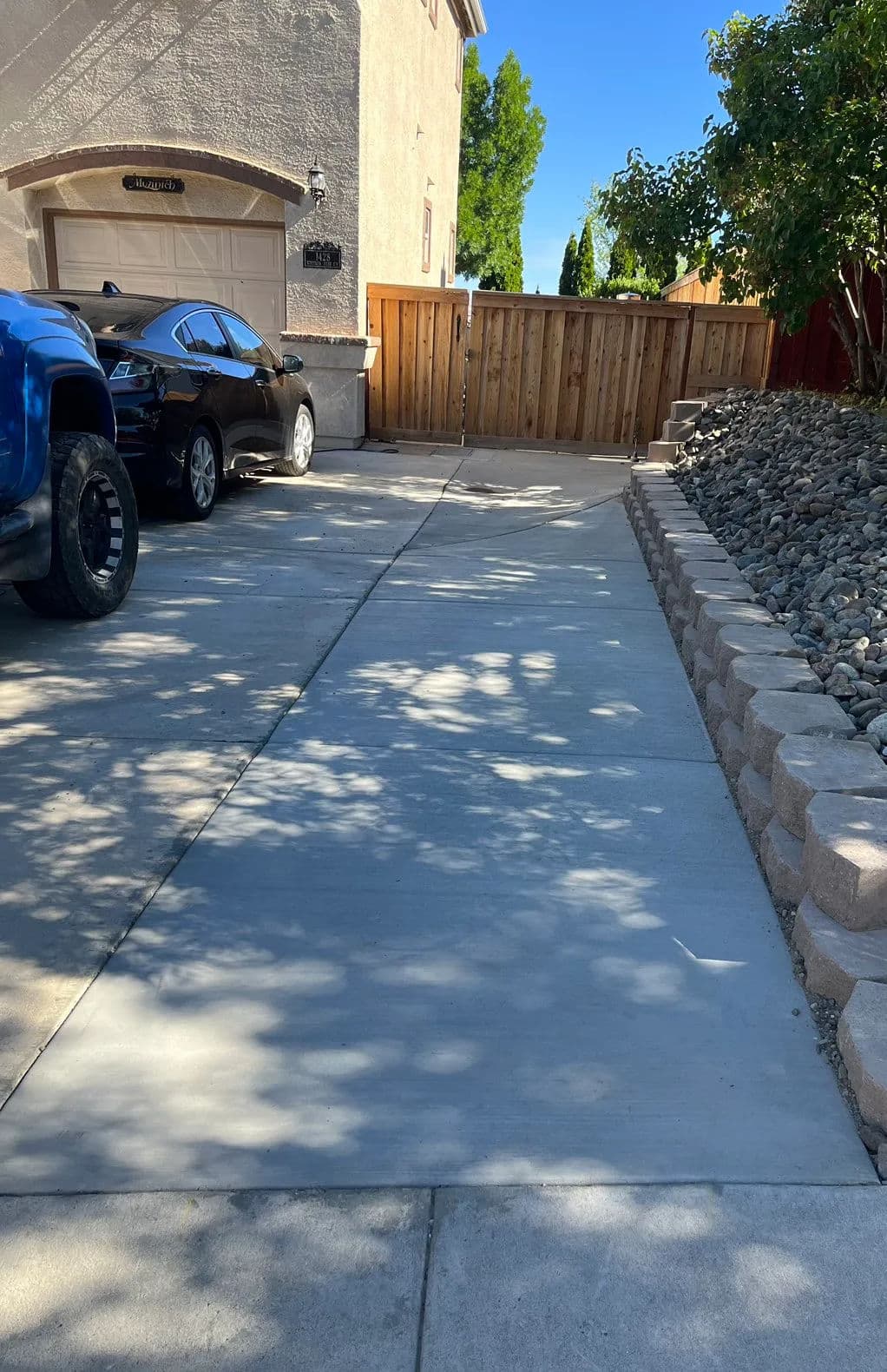 Concrete driveway leading to a fenced yard with parked cars and landscaped stones.