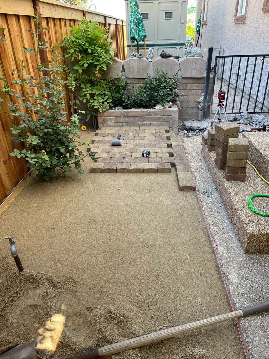 Garden landscaping project with paver stones, sand base, and greenery in urban backyard.