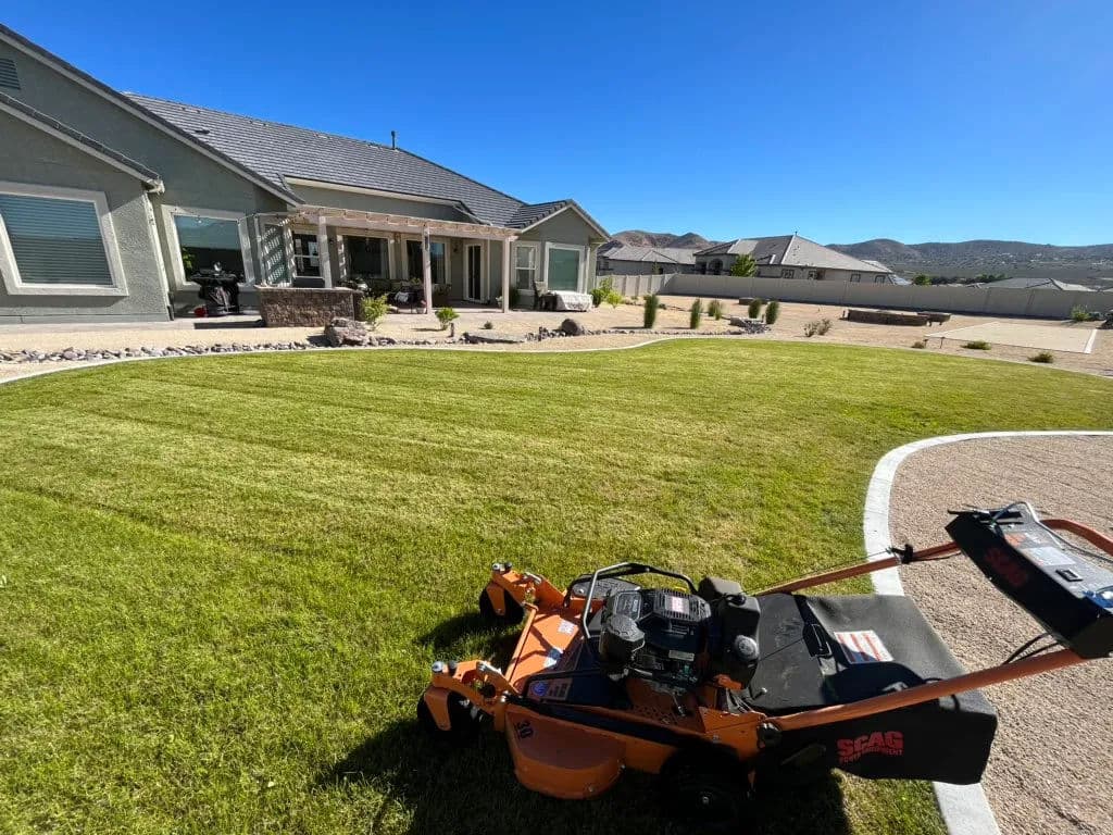 Lawn mower on neatly trimmed grass in front of a modern house with blue sky.