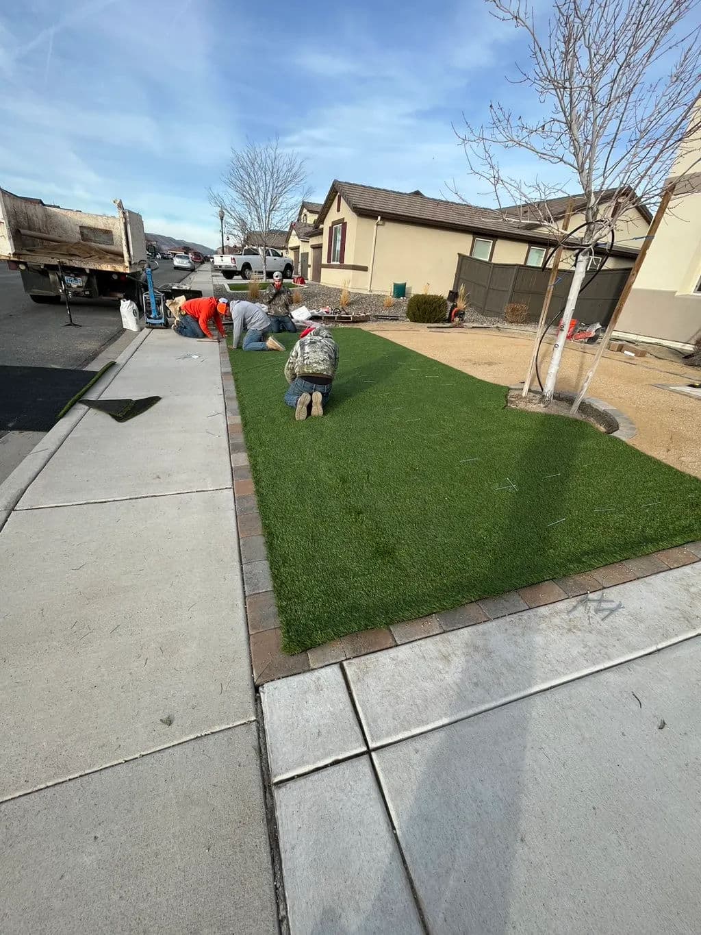 Landscapers installing artificial turf on a residential lawn, enhancing outdoor aesthetics.