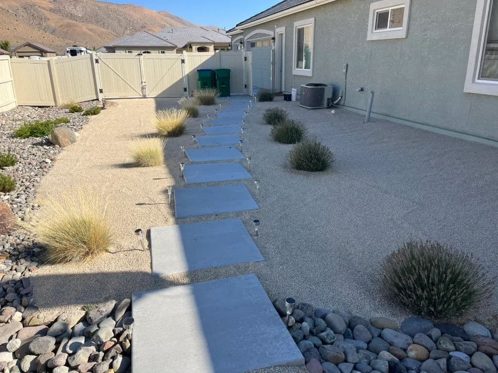 Modern backyard landscape with stone path, gravel, decorative grasses, and mountain backdrop.