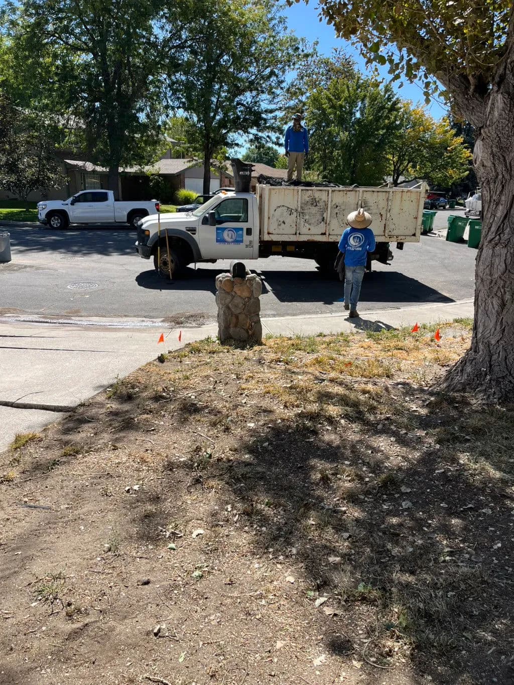 Workers in blue shirts loading debris into a truck in a residential area with trees.