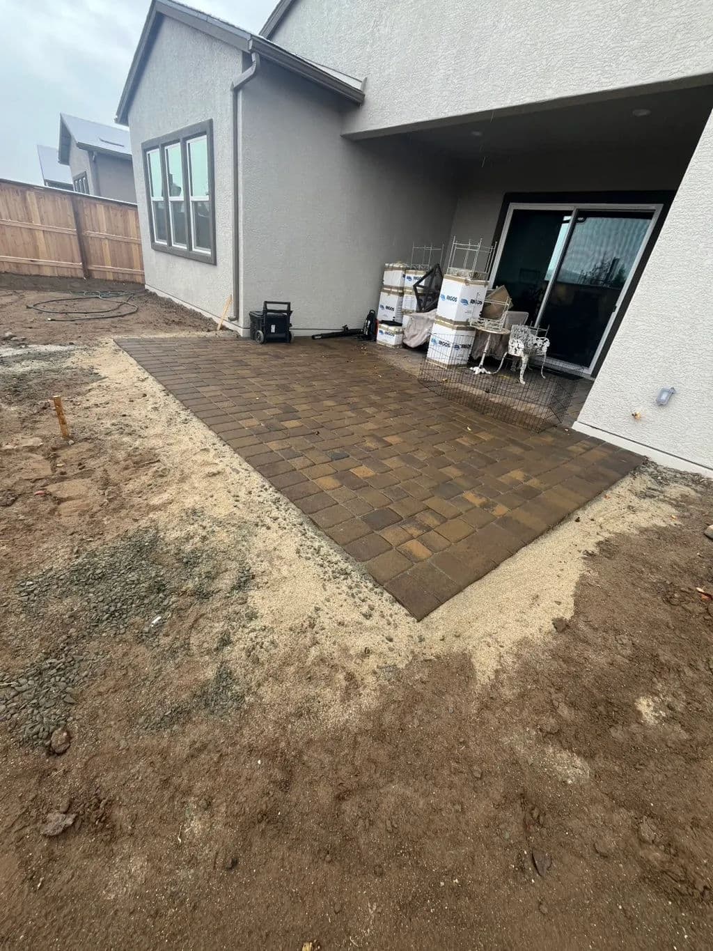 Patio area with new paver stones, construction materials, and gravel in a backyard setting.