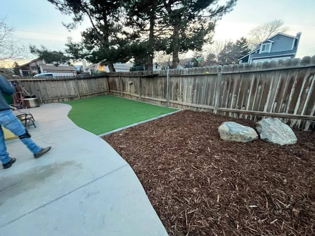 Lush green turf area with mulch and rocks in a backyard, fenced for privacy.